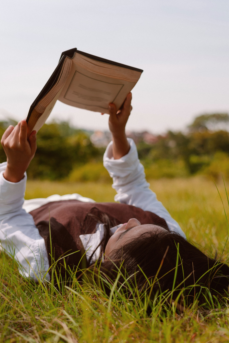 Woman Reading Book While Lying on the Field